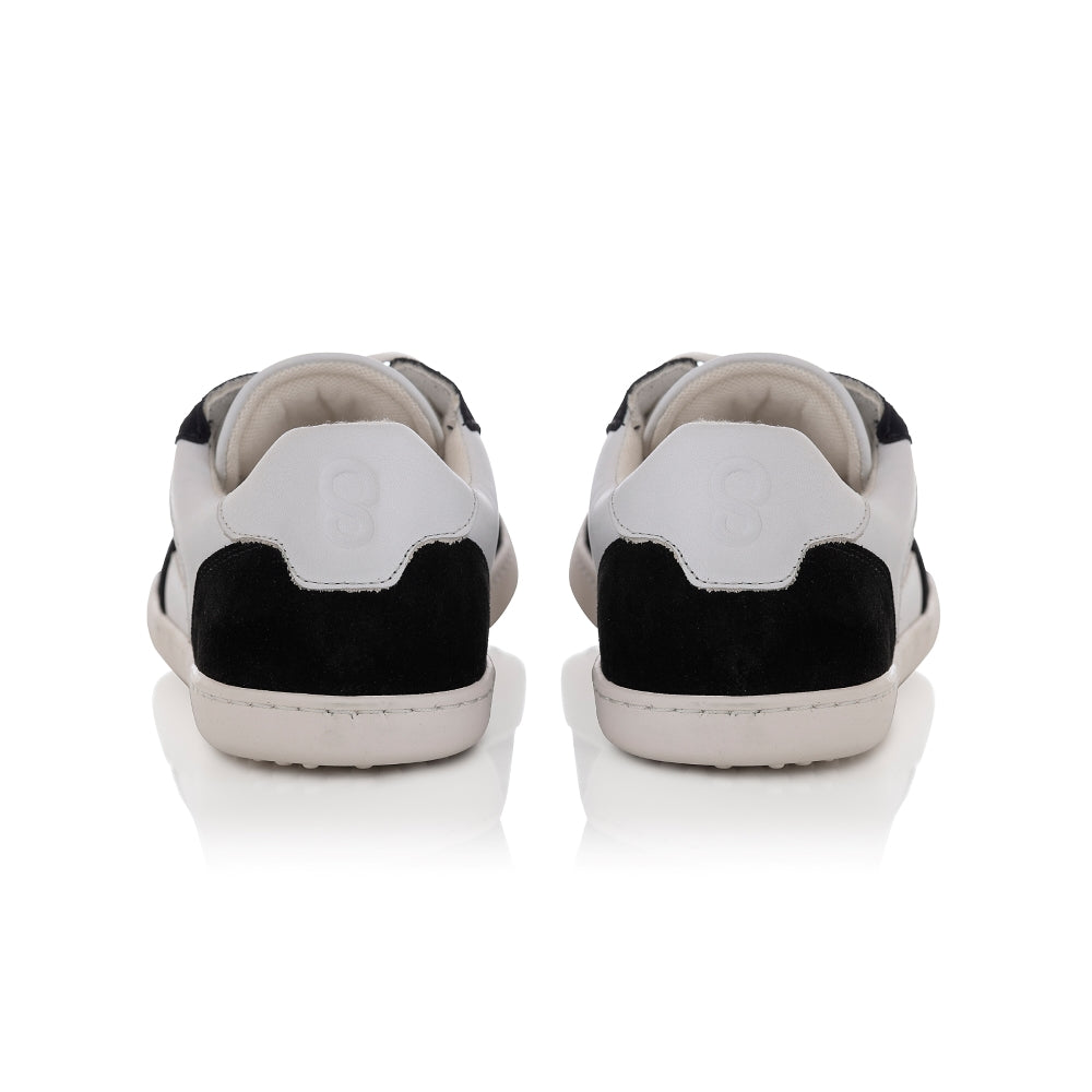 A photo of Shapen ReWind leather sneakers in white & black. Shoes are a classic chunky sneaker design with black suede color blocks surrounding the toe guard, laces, and heels. Both shoes are shown here from the back against a white background. #color_black-white