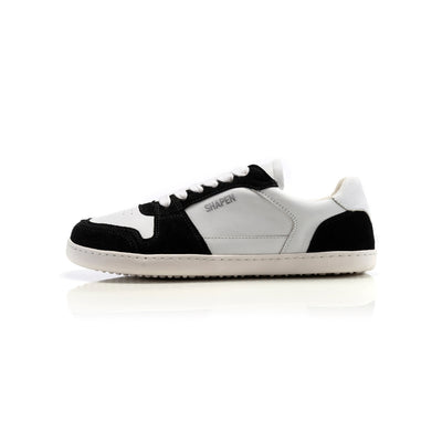 A photo of Shapen ReWind leather sneakers in white & black. Shoes are a classic chunky sneaker design with black suede color blocks surrounding the toe guard, laces, and heels. Left shoe is shown facing left here against a white background. #color_black-white