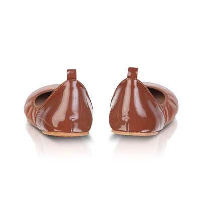 A photo of Shapen Tulip flats in cognac made of leather and rubber soles. Shoes have a gentle elastic around the perimeter of the opening, a patent leather heel cup, and an optional patent leather ankle strap. Both shoes are shown here without the ankle strap from the back against a white background. #color_cognac