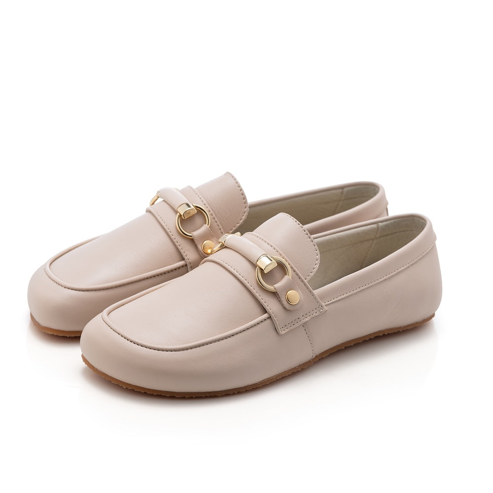 Beige leather Shapen Versa loafers. Shoes are a classic loafer design with a leather decoration capped by gold metal rings across the foot and tan rubber soles glued on. Both shoes are shown facing diagonally left against a white background. #color_beige