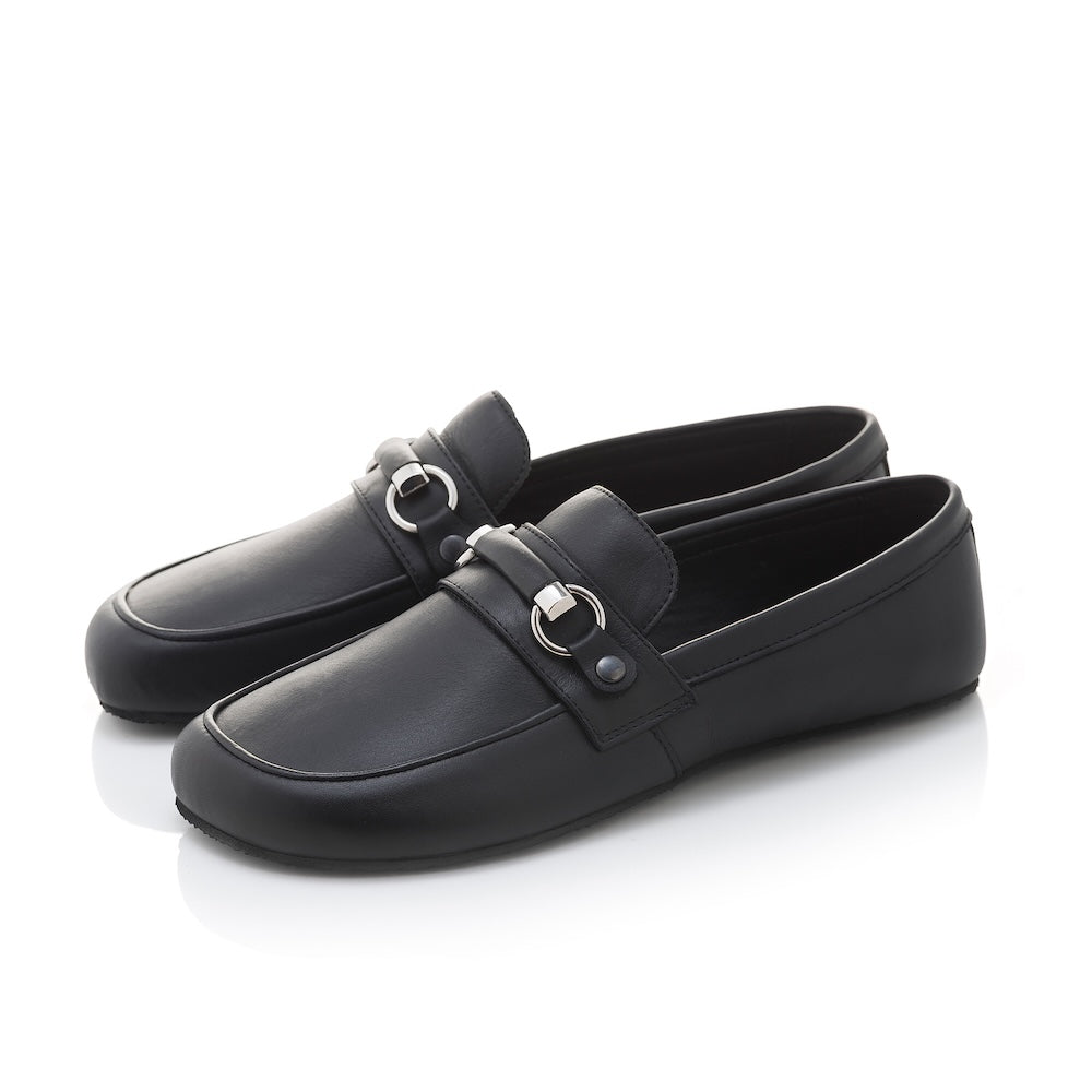 Black leather Shapen Versa loafers. Shoes are a classic loafer design with a leather decoration capped by silver metal rings across the foot and black rubber soles glued on. Both shoes are shown facing diagonally left against a white background. #color_black