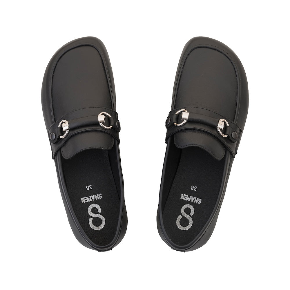 Black leather Shapen Versa loafers. Shoes are a classic loafer design with a leather decoration capped by silver metal rings across the foot and black rubber soles glued on. Both shoes are shown from above against a white background. #color_black