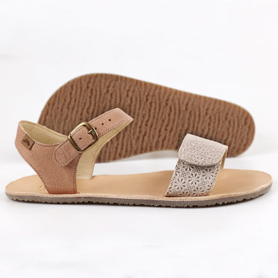 Tikki Vibe tan and ivory leather sandals with a tan footbed and gum soles. A thick leather ivory velcro strap with a pressed floral patterm secures the foot at the toes with a slimmer tan ankle buckle-closure strap in the back. Right shoe is shown here facing right with the left shoe sole shown in the background facing left against a white background. #color_claire-leather