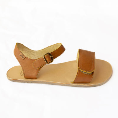 Tikki Vibe brown leather sandals with a tan footbed and soles. A thick velcro strap secures the foot at the toes with a slimmer ankle buckle-closure strap in the back. Right shoe is shown here facing right against a white background. #color_cream-leather