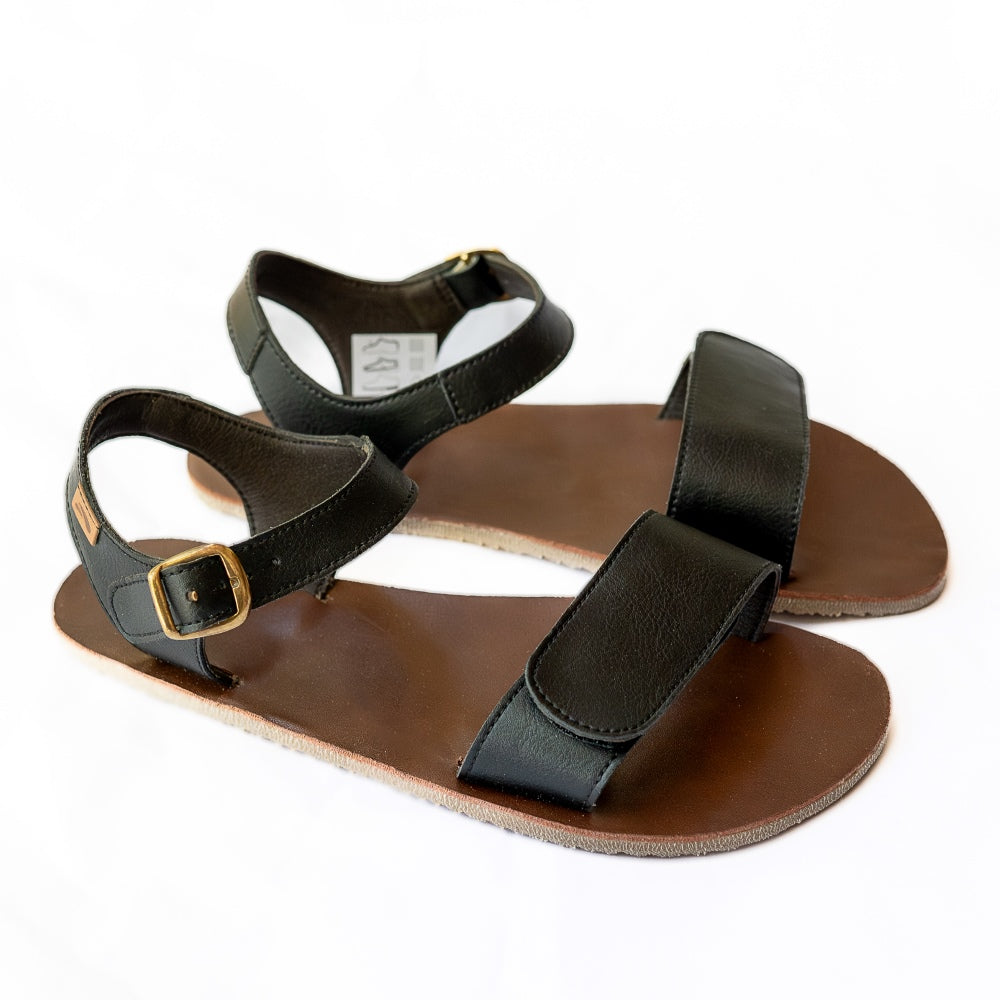 Tikki Vibe black vegan sandals with tan soles and a brown footbed. A thick velcro strap secures the foot at the toes with a slimmer ankle buckle-closure strap in the back. Both shoes are shown here facing diagonally right against a white background. #color_onyx-vegan