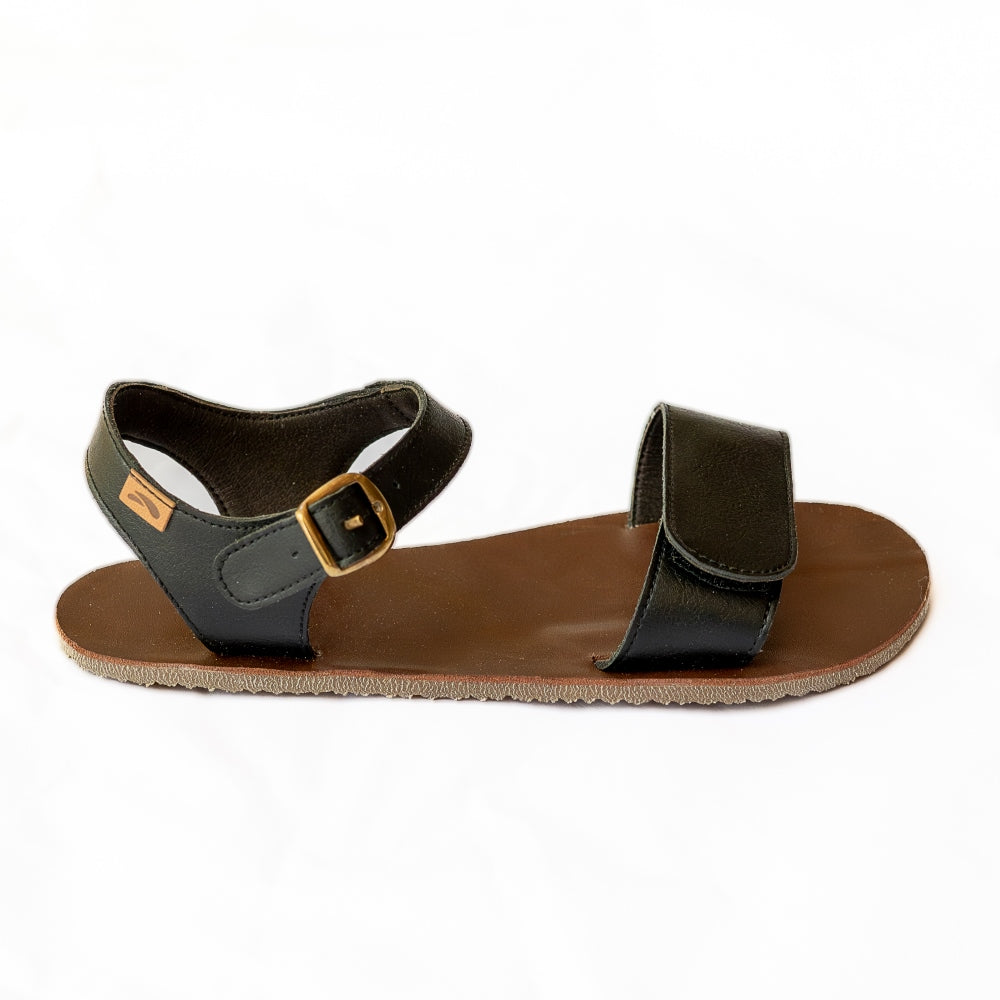 Tikki Vibe black vegan sandals with tan soles and a brown footbed. A thick velcro strap secures the foot at the toes with a slimmer ankle buckle-closure strap in the back. Right shoe is shown here facing right against a white background. #color_onyx-vegan