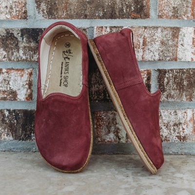 A photo of Yasemin Leather loafers Designed by Anya with a leather upper and tan rubber soles. The loafers are a mauve nubuck color and have a small curve up on the top of the foot for design. Both loafers are shown leaning against a brick wall with the right shoe facing to the right side both resting on cement. #color_mauve-nubuck