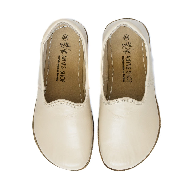A photo of Yasemin Leather loafers Designed by Anya with a leather upper and tan rubber soles. The loafers are a smooth beige leather upper and have a small curve up on the top of the foot for design. Both loafers are shown from the top facing down against a white background. #color_beige