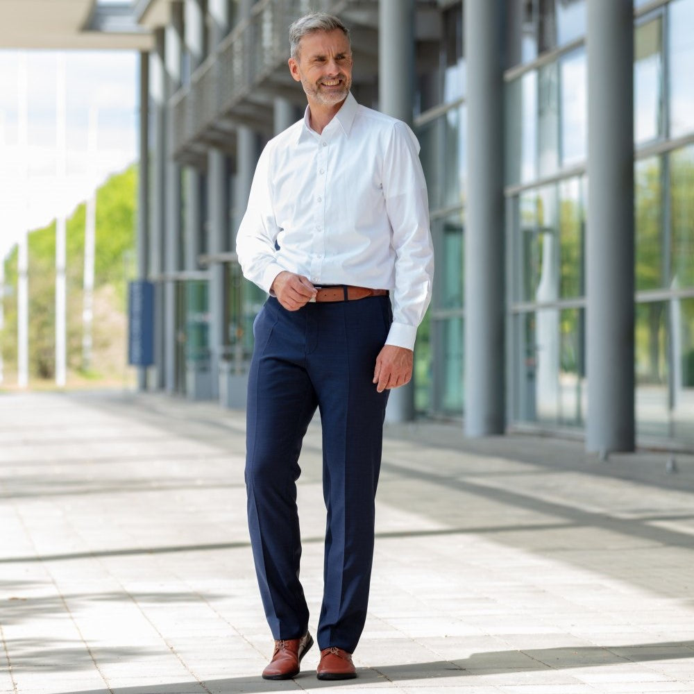 Cognac Zaqq Peaq leather dress shoes with coganc laces and black rubber soles. Both shoes are shown form the front a man with short grey hair, wearing navy dress slacks, a cognac belt, and a white dress shirt standing on a square paver path beside a tall building. #color_cognac