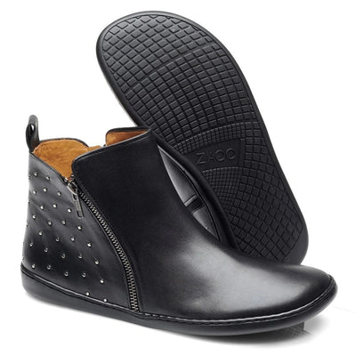 All black leather Zaqq Qlare boot with tan leather lining and a black pull tab. The front of the boot is plain while the back has small silver studs with a silver diagonal zipper on the outside ankle. Right shoe is shown facing diagonally right against a white background while the left shoe is propped up showing the sole behind it. #color_black