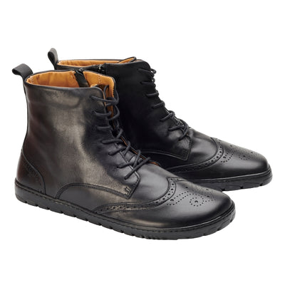 Black Zaqq Quintic Brogue leather, unlined boots with side zippers. Shoes go over the ankles, a pull tab at the top back, have tan lining, and have a brogue design on the toebox. Both shoes are shown here facing right against a white background. #color_black