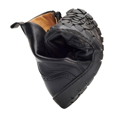 Black Zaqq Quintic Brogue leather, unlined boots with side zippers. Shoes go over the ankles, a pull tab at the top back, have tan lining, and have a brogue design on the toebox. One shoe is shown here rolled against a white background. #color_black