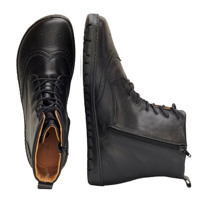 Black Zaqq Quintic Brogue leather, unlined boots with side zippers. Shoes go over the ankles, a pull tab at the top back, have tan lining, and have a brogue design on the toebox. Left shoe is shown from above next to the right shoe laying on its side against a white background. #color_black