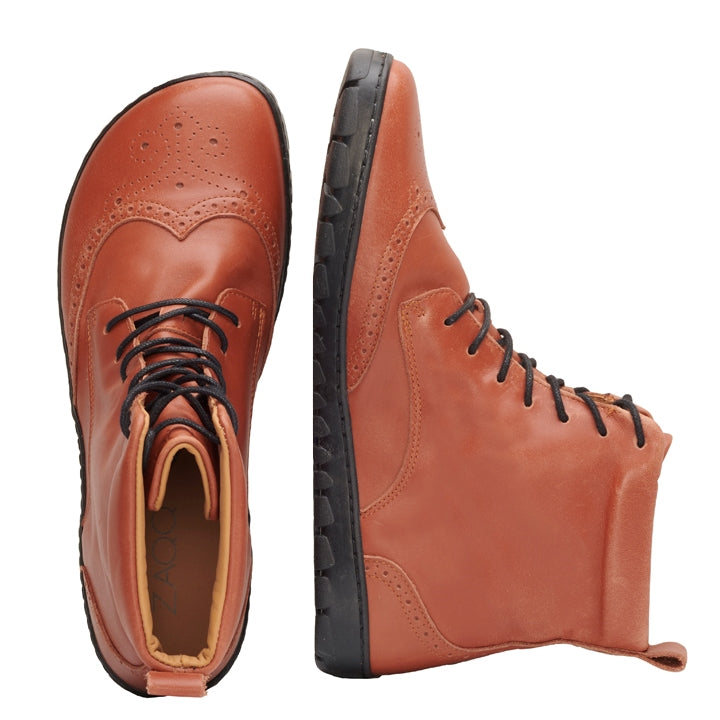 Cognac Zaqq Quintic Brogue leather, unlined boots. Shoes go over the ankles, have black soles and laces, a pull tab at the top back, and have a brogue design on the toebox. Left shoe is shown from above next to the right shoe laying on its side against a white background. #color_cognac