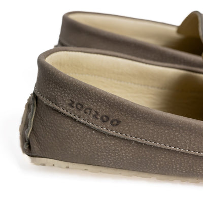A photo of the Zeazoo Cheetah loafers made from a natural nappa leather upper on a tan Vibram sole. The loafers are stone in color and have a silver metal detail across the top of the foot. Both loafers are shown together from the right side on a white background with a focus on the branding on the outside heel. #color_stone