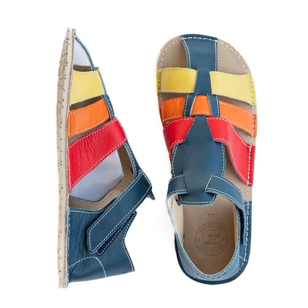 A photo of the Zeazoo Marlin lids leather play sandals. The sandals are navy blue in color and have yellow, orange, and red straps weaved across the top of the shoe, and a velcro closure around the ankle. The left shoe is shown from the left and the right show is shown from above on a white background. #color_navy-yellow-orange-red