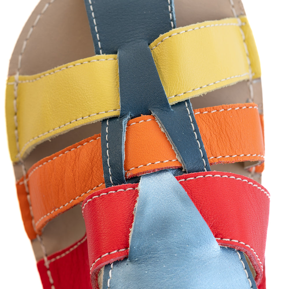 A photo of the Zeazoo Marlin lids leather play sandals. The sandals are navy blue in color and have yellow, orange, and red straps weaved across the top of the shoe, and a velcro closure around the ankle. A close up of the colored straps is shown from above on a white background. #color_navy-yellow-orange-red