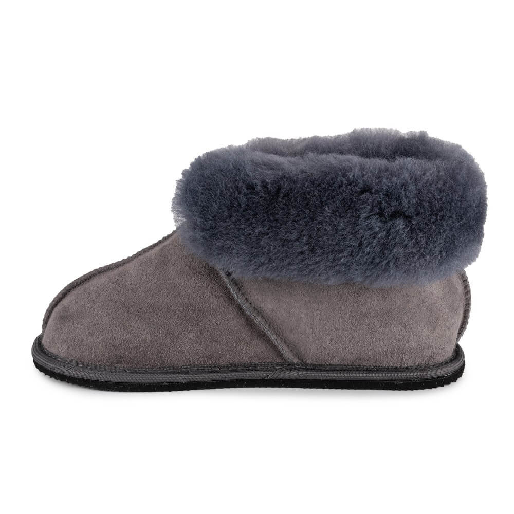 Grey colored Zeezoo Shaun hand made suede, sheepskin, and tan rubber slippers. The slippers are composed of 4 panels sewn together with seams on the sides, back, and top. Fur lining folds over at the ankle. Right slipper is shown facing left against a white background. #color_grey