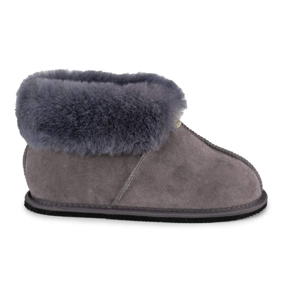 Grey colored Zeezoo Shaun hand made suede, sheepskin, and tan rubber slippers. The slippers are composed of 4 panels sewn together with seams on the sides, back, and top. Fur lining folds over at the ankle. Right slipper is shown facing right against a white background. #color_grey