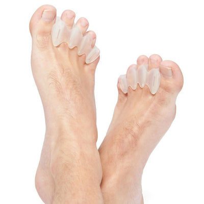 A photo of correct toes clear toe spacers made from silicone. A man’s feet are shown crossed at the ankles while wearing the correct toes against a white background. 