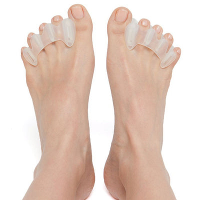 A photo of correct toes clear toe spacers made from silicone. A woman’s feet are shown  from the ankle down with her heels are resting on the ground while her feet are facing up while wearing the correct toes against a white background. 