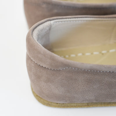 A photo of Yasemin Leather loafers Designed by Anya with a leather upper and tan rubber soles. The loafers are a taupe nubuck color and have a small curve up on the top of the foot for design. A close up is shown of the right shoes heel which shows the tan color inside against a white background. #color_taupe-nubuck