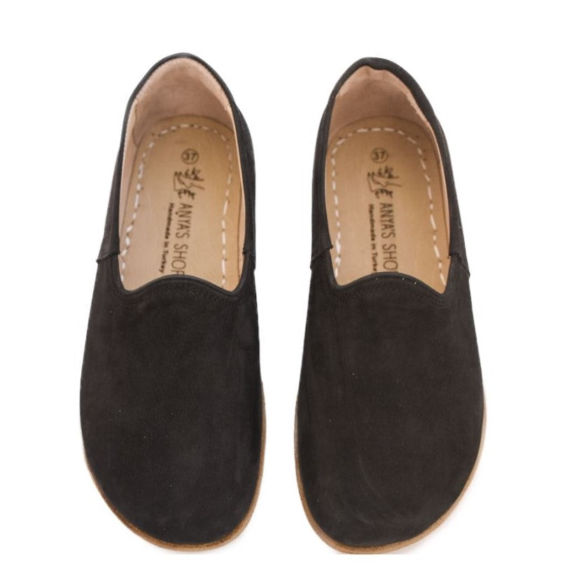 A photo of Yasemin Leather loafers Designed by Anya with a leather upper and tan rubber soles. The loafers are a black color with a nubuck leather upper and have a small curve up on the top of the foot for design. Both loafers are shown from the top facing down against a white background. #color_black-nubuck