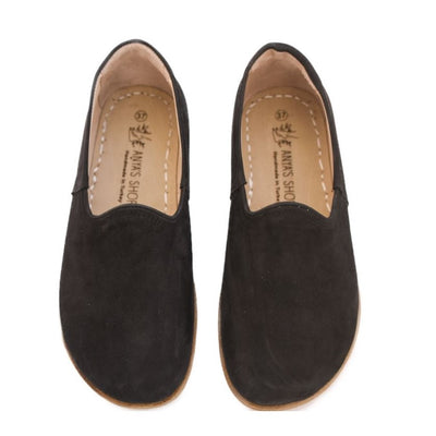 A photo of Yasemin Leather loafers Designed by Anya with a leather upper and tan rubber soles. The loafers are a black color with a nubuck leather upper and have a small curve up on the top of the foot for design. Both loafers are shown from the top facing down against a white background. #color_black-nubuck