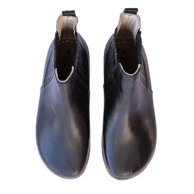 A photo of designed by Anya Lila boots made from leather and rubber soles. The boots are black in color, they are a Chelsea boot style with a lined detailed panel on the sides. Both boots are shown beside each other from above against a white background. #color_black-smooth-leather