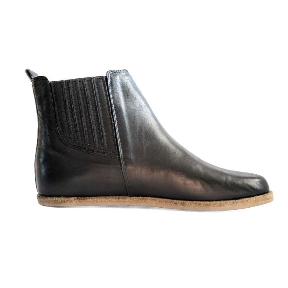 A photo of designed by Anya Lila boots made from leather and rubber soles. The boots are black in color, they are a Chelsea boot style with a lined detailed panel on the sides. One boot is shown from the right side against a white background. #color_black-smooth-leather