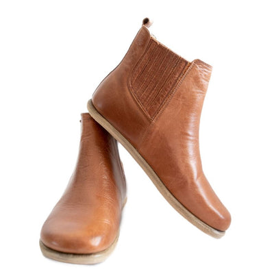 A photo of designed by Anya Lila boots made from leather and rubber soles. The boots are black in color, they are a Chelsea boot style with a lined detailed panel on the sides. Both boots are shown the right boot is shown from the front angled slightly to the left, the heel of the is resting on the left boot and facing downward against a white background. #color_brown