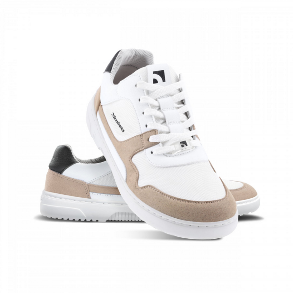 A photo of Barebarics Zing sneakers made with a leather upper and a rubber sole. The sneakers are a white and beige color with perforated spots on the top of the toe box and barebarics branding on the tongue and side. They also have black at the top of the heel. Both shoes are shown, the left shoe is behind the right. The right shoes heel is leaning up against the left shoe showing the right shoe from the front facing down against a white background. #color_white-beige