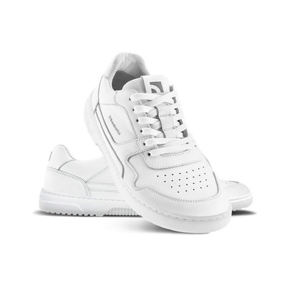 A photo of Barebarics Zing sneakers made with a leather upper and a rubber sole. The sneakers are a white color with perforated spots on the top of the toe box and barebarics branding on the tongue and side.  Both shoes are shown, the left shoe is behind the right. The right shoes heel is leaning up against the left shoe showing the right shoe from the front facing down against a white background. #color_white