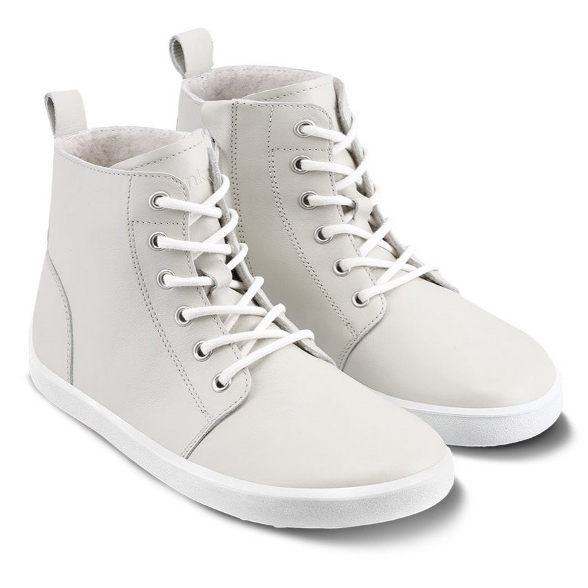 A photo of Be Lenka Atlas ankle zip up boots made from smooth leather and rubber soles. The boots are cream in color with white laces, zippers, a pull tab in the back, and lined with felt. Both boots are shown diagonally from the right side against a white background. #color_black