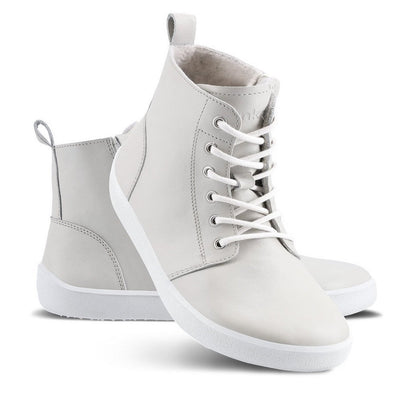 A photo of Be Lenka Atlas ankle zip up boots made from smooth leather and rubber soles. The boots are cream in color with white laces, zippers, a pull tab in the back, and lined with felt. Left boot shown from the left side with the right boot's heel resting diagonally on the left against a white background. #color_cream