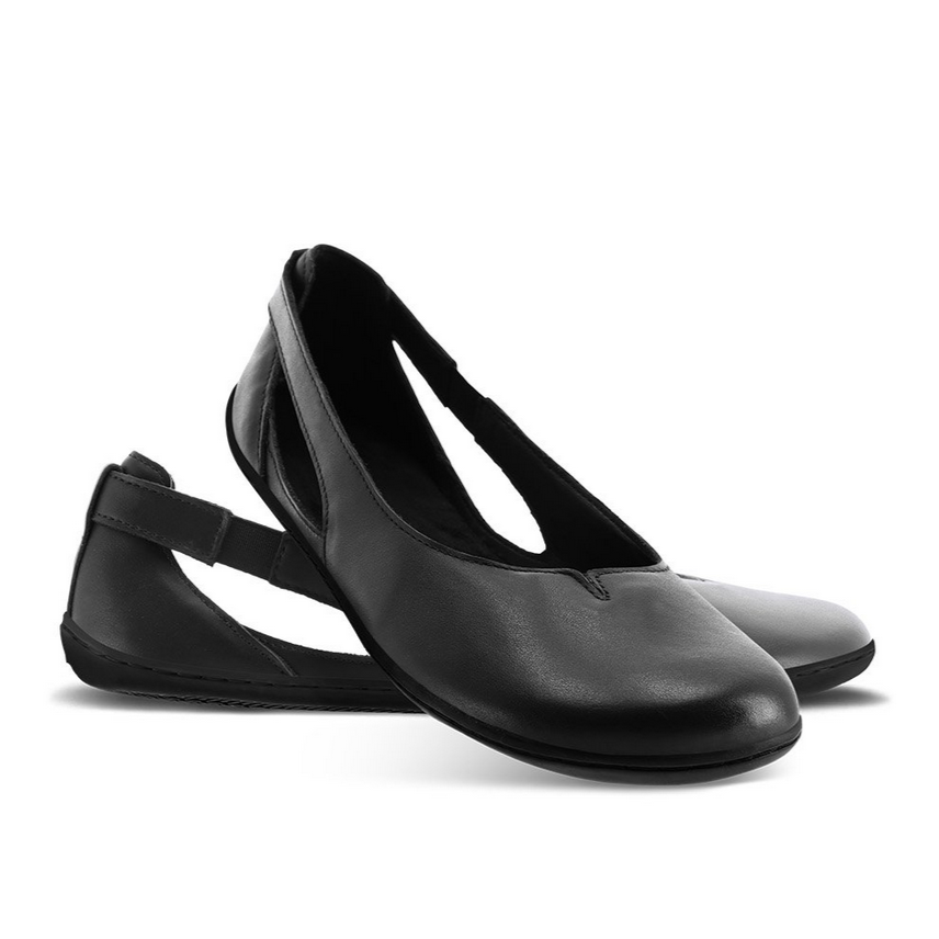A photo of Be Lenka Bellissima flats with a leather upper and rubber soles. The flats are a black color with a small stitching V detail in the front and a cut out design on the sides. Both flats are shown facing right the right flat is in front with its heel leaning on the left shoe against a white background. #color_black