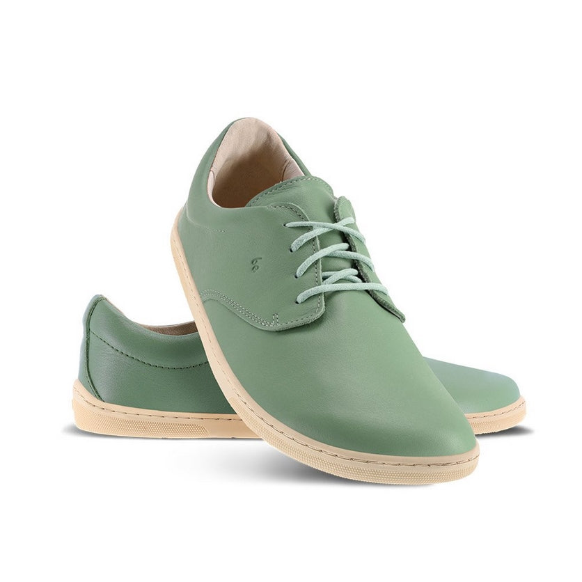 A photo of Sage Green Be Lenka Cityscape Simple Leather Lace Up shoes with beige soles. Left shoe is shown from the right with the right shoe propped up on the left to show the top of the shoe. Background is white. #color_sage-green