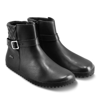 A photo of Be Lenka Diva boots in all black. Boots are made from smooth black leather. A quilted leather design is present in the back, a silver buckle on the side, a strap around the ankle, and a zipper. Both shoes are shown diagonally from the front right against a white background. #color_all-black