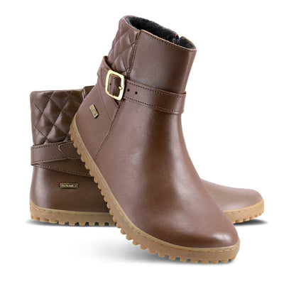 A photo of Be Lenka Diva boots in dark brown with tan soles. Boots are made from dark brown leather. A quilted leather design is present in the back, a silver buckle on the side, a strap around the ankle, and a zipper. Left shoe is shown from the right side with the left boot propped up against it with a white background. #color_dark-brown