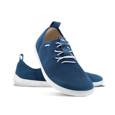 A photo of Dark Blue Be Lenka Elevate Mesh Sneaker shoes with white soles and white elastic laces. Left shoe is shown from the right with the right shoe propped up on the left to show the top of the shoe. Background is white. #color_dark-blue
