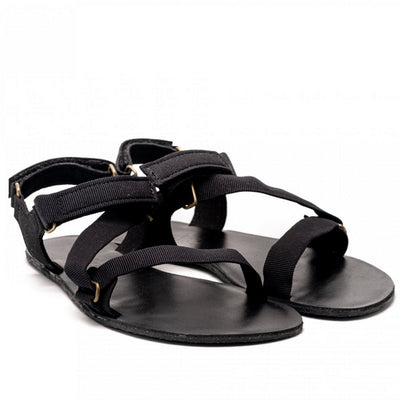 A photo of Black Be Lenka Flexi Sandals made with fabric straps with velcro and a tan leather topped rubber soles. The sandals are a black color and have straps that cross the front of the foot and continue around the mid-foot, ankle, and heel. Both sandals are shown beside each other facing forward and slightly angled to the right against a white background. #color_black