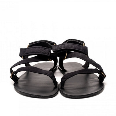 A photo of Black Be Lenka Flexi Sandals made with fabric straps with velcro and a tan leather topped rubber soles. The sandals are a black color and have straps that cross the front of the foot and continue around the mid-foot, ankle, and heel. Both sandals are shown from the front beside each other against a white background in this photo. #color_black