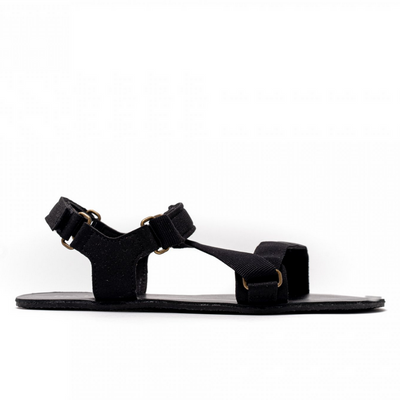 A photo of Black Be Lenka Flexi Sandals made with fabric straps with velcro and a tan leather topped rubber soles. The sandals are a black color and have straps that cross the front of the foot and continue around the mid-foot, ankle, and heel. One sandal is shown from the right side against a white background in this photo. #color_black