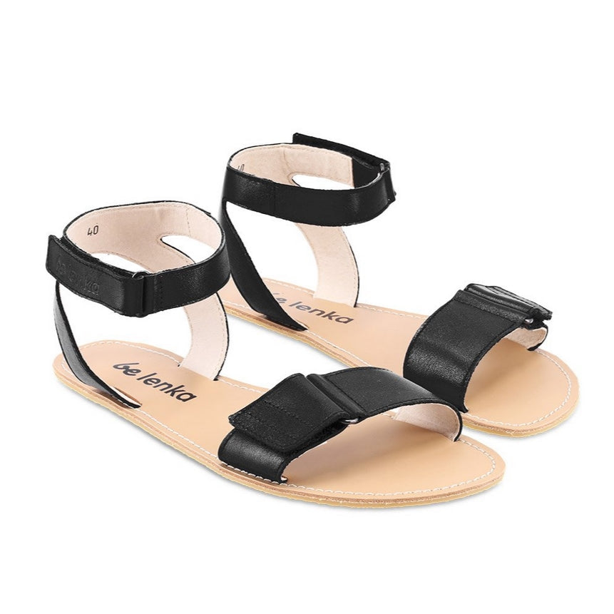 A photo of black leather Be Lenka Iris Sandals. An adjustable strap wraps around the ankle once with an open heel while a thicker adjustable strap goes over the toes. Sandals are shown diagonally from the front right side against a white background. #color_black