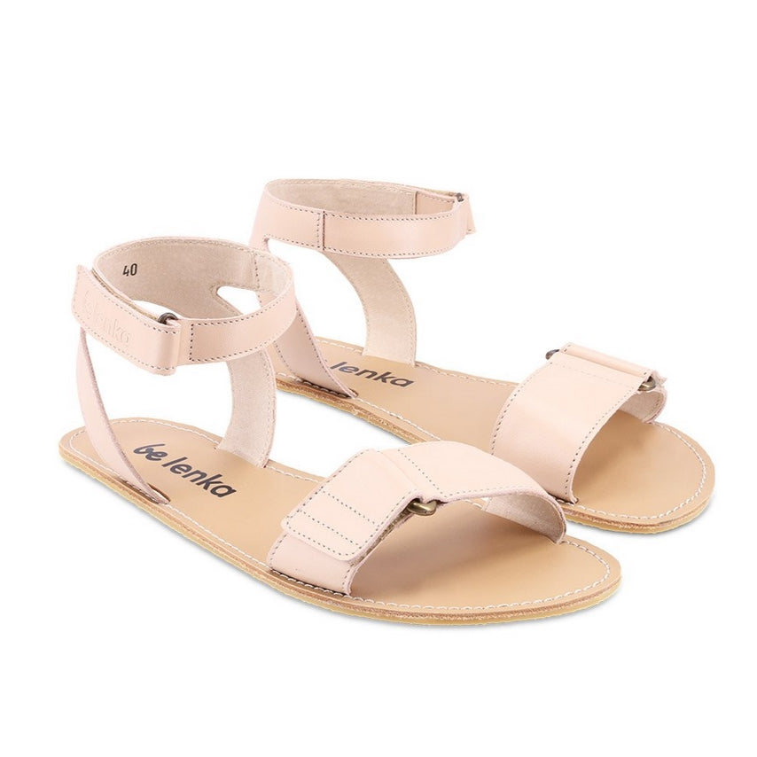 A photo of beige leather Be Lenka Iris Sandals. An adjustable strap wraps around the ankle once with an open heel while a thicker adjustable strap goes over the toes. Sandals are shown diagonally from the front right side against a white background. #color_nude