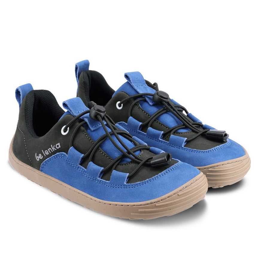 A photo of Be Lenka Xplorer kids shoes in blue and olive black nubuck leather with gum soles and black laces. The black color goes from the heel to the front of the shoe with a blue tongue, pull tab, and around the side and front edges of the toe box. Elastic laces are laced through blue tabs attached to the blue leather accents on sides and end at the black color on either side of the tongue. #color_blue-olive-black