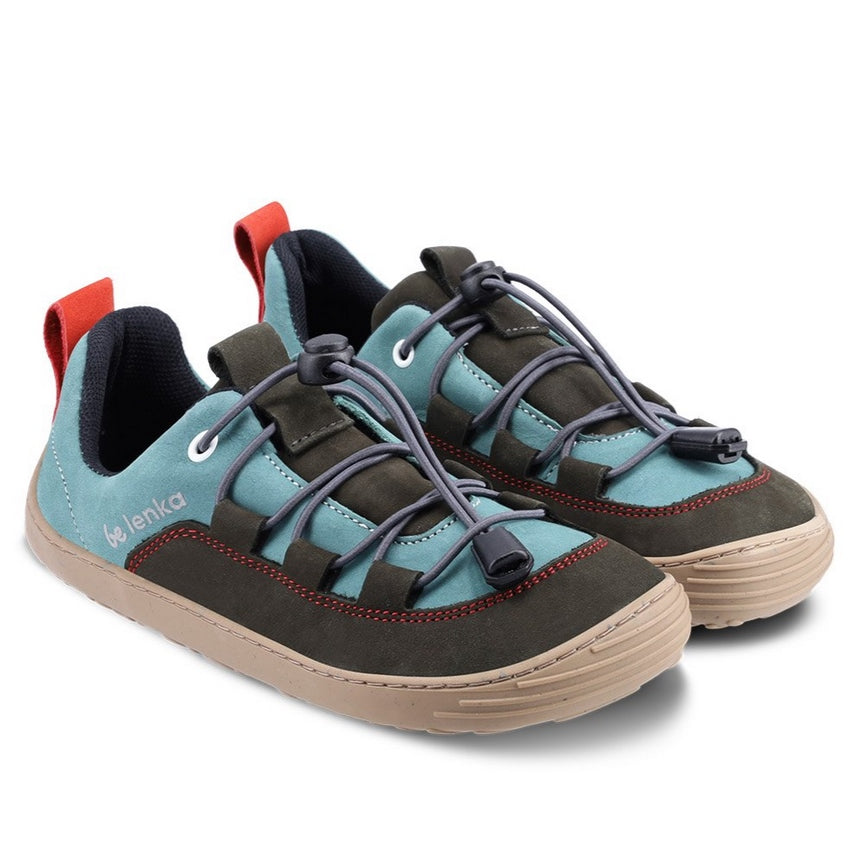 A photo of Be Lenka Xplorer kids shoes in olive black and sage green nubuck leather with gum soles and dark grey laces. The green color goes from the heel to the front of the shoe with a black tongue, pull tab, and around the side and front edges of the toe box. Elastic laces are laced through black tabs attached to the black leather accents on sides and end at the green color on either side of the tongue. #color_olive-black-sage-green
