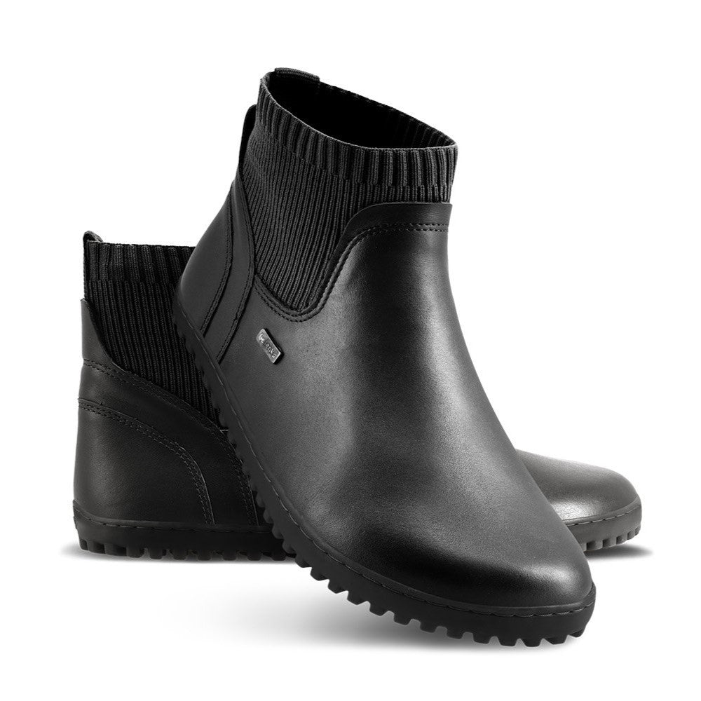 A photo of Be Lenka Mojo boots in black. Boots are made from smooth black leather and a knit opening hugging around the ankle. Left shoe is shown from the right side with the left boot propped up against it with a white background. #color_black