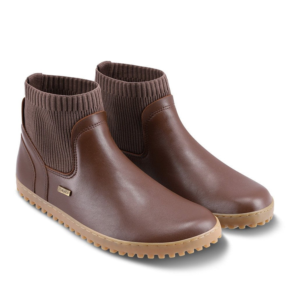 A photo of Be Lenka Mojo boots in dark brown with tan soles. Boots are made from smooth black leather and a knit opening hugging around the ankle. Both shoes are shown diagonally from the front right against a white background. #color_dark-brown