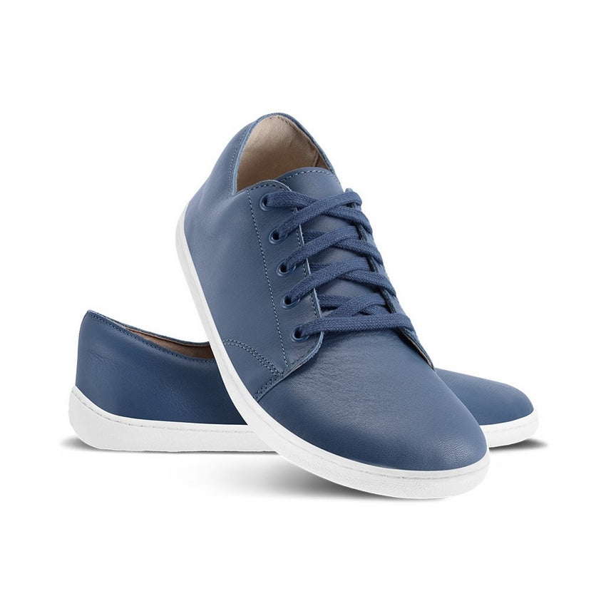 A photo of Insignia Blue Be Lenka Prime 2.0 Simple Leather Sneakers with white soles. Left shoe is shown from the right with the right shoe propped up on the left to show the top of the shoe. Background is white. #color_insignia-blue